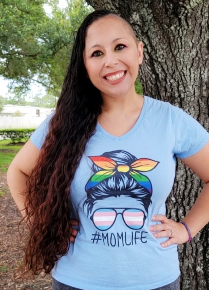 A woman wearing a shirt that says #MomLife, with a rainbow and transgender flag