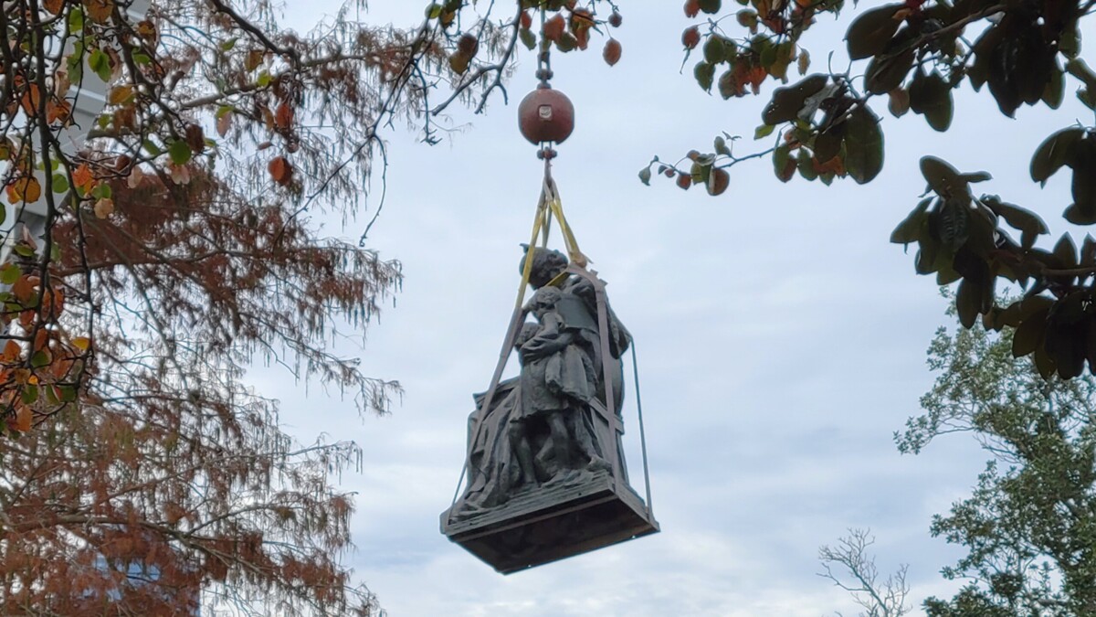 The statue of a mother and child honoring "The Women of our Southland 1861-1865" hangs from a crane Wednesday, Dec. 27, 2023, after its removal from a monument in Springfield Park. | Dan Scanlan, WJCT News 89.9