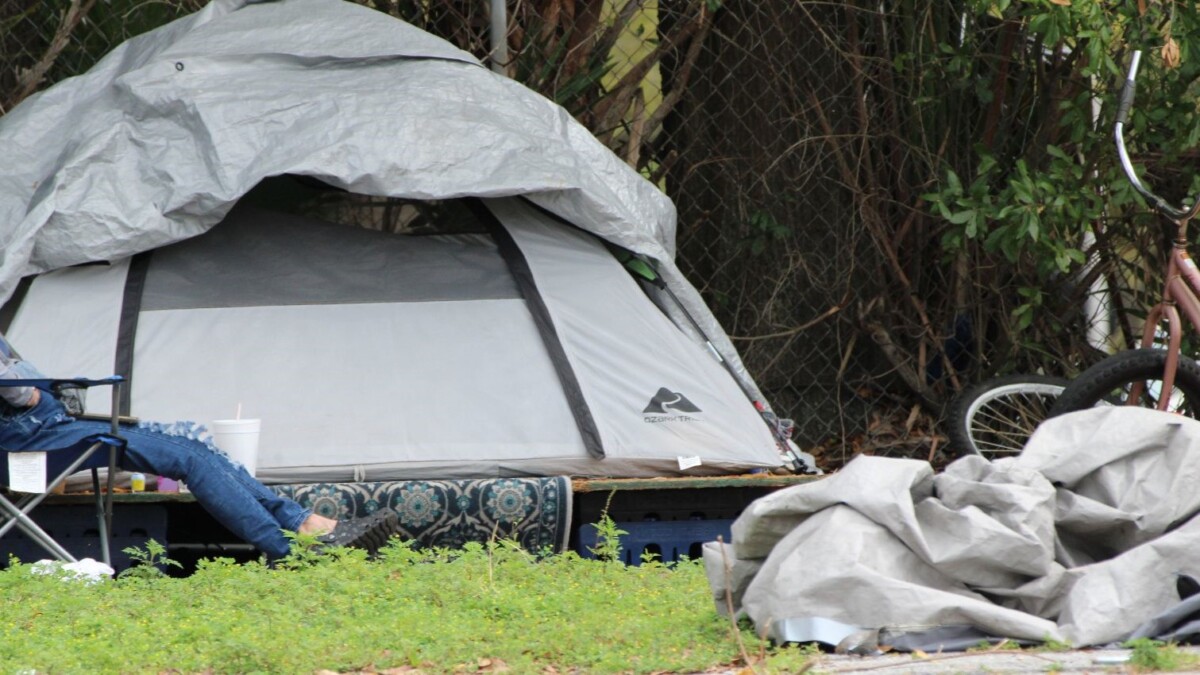A person sits near their tent in an empty lot near Ashley and Clay streets in Downtown Jacksonville on March 8, 2024. l Casmira Harrison, Jacksonville Today.
