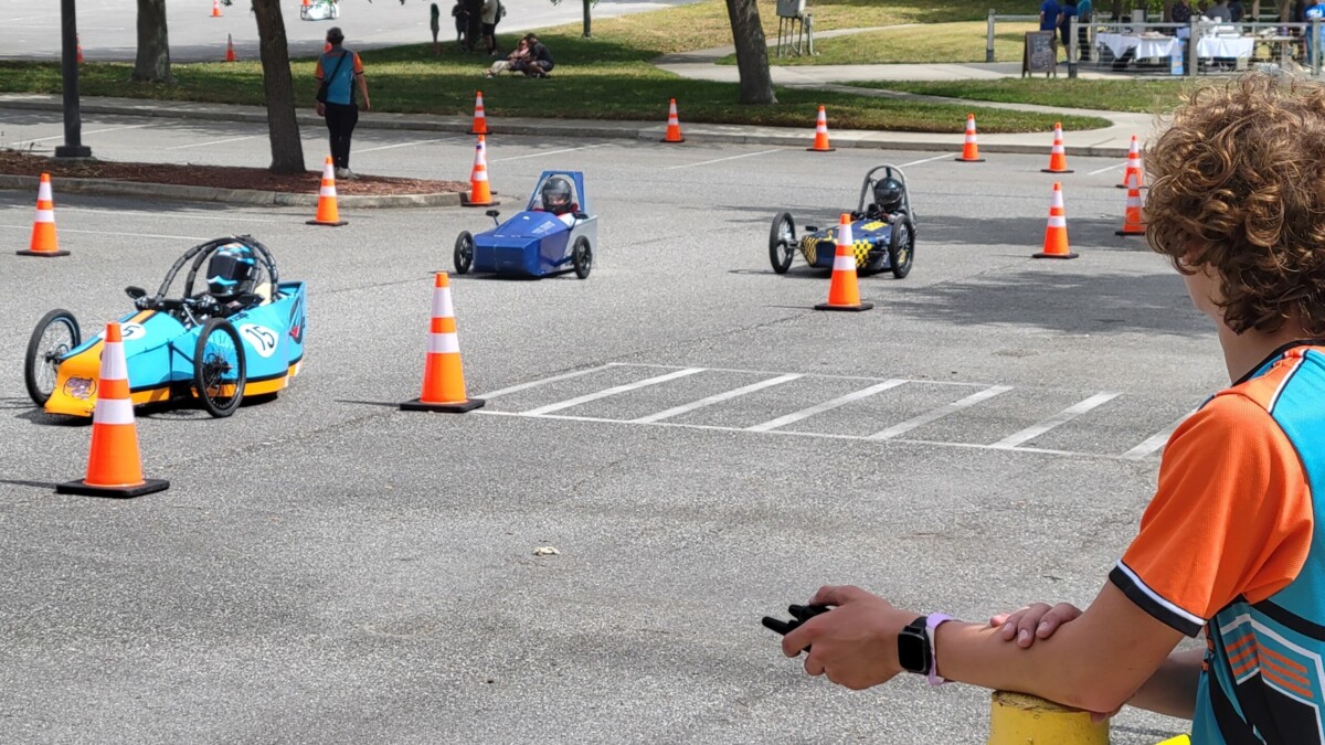 Three EV race cars zip past a course worker Saturday, April 27, 2024, during a race at Florida State College at Jacksonville. | Dan Scanlan, Jacksonville Today