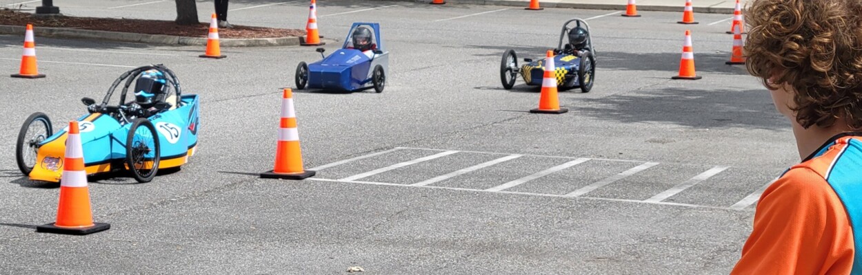 Three EV race cars zip past a course worker Saturday, April 27, 2024, during a race at Florida State College at Jacksonville. | Dan Scanlan, Jacksonville Today