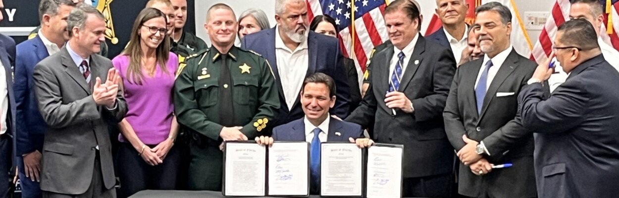 Flanked by law enforcement officers and legislators at the St. Johns County Sheriff's Office, Gov. Ron DeSantis shows bills he signed Friday, April 12, 2024. | Noah Hertz, Jacksonville Today.