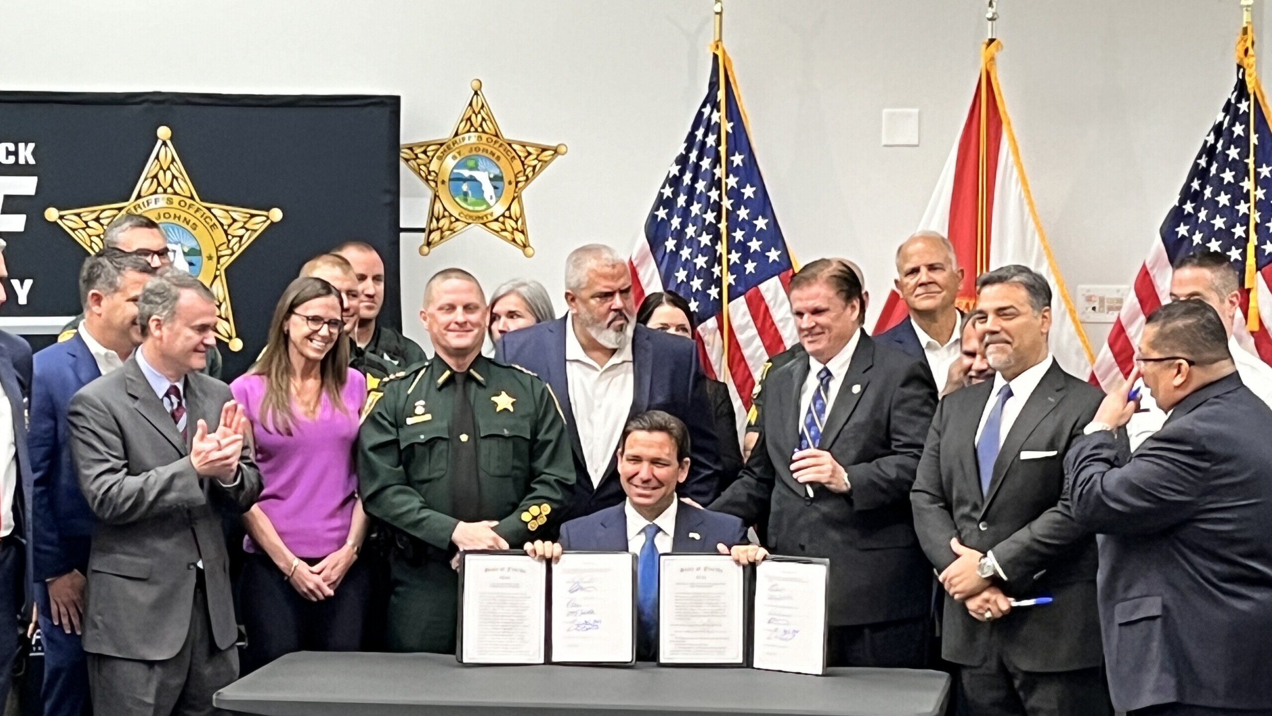 Flanked by law enforcement officers and legislators at the St. Johns County Sheriff's Office, Gov. Ron DeSantis shows bills he signed Friday, April 12, 2024. | Noah Hertz, Jacksonville Today.
