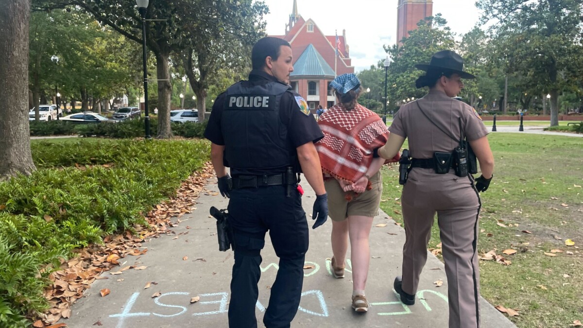 A University of Florida police officer and a Florida Highway Patrol trooper walk a handcuffed protester away from the site on the university's campus, where law enforcement arrested nine pro-Palestinian protesters April 29, 2024. | Vivienne Serret, Fresh Take Florida
