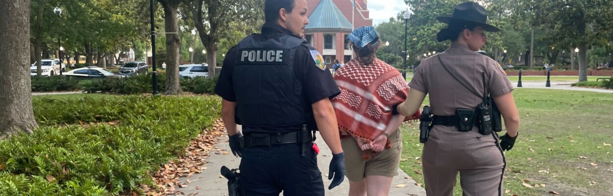 A University of Florida police officer and a Florida Highway Patrol trooper walk a handcuffed protester away from the site on the university's campus, where law enforcement arrested nine pro-Palestinian protesters late Monday, April 29, 2024. | Vivienne Serret, Fresh Take Florida