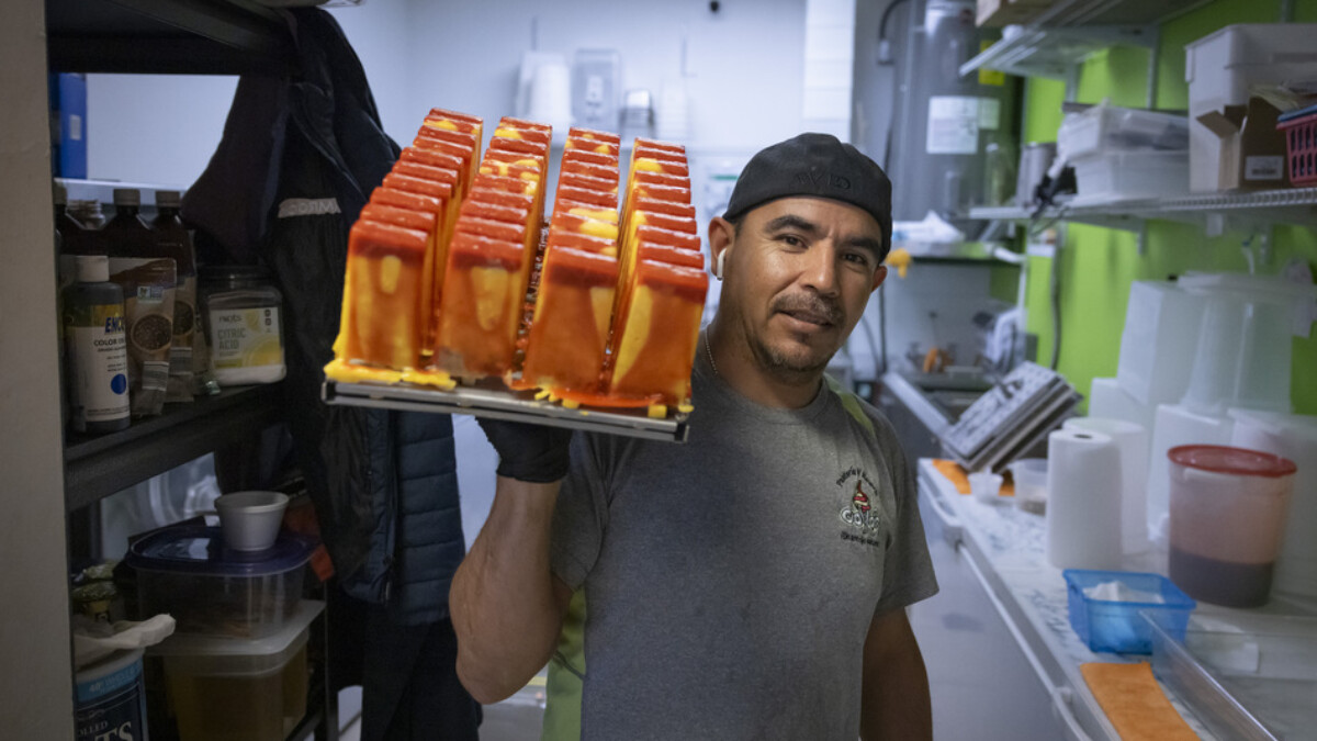 Manuel Vazquez, owner of Coya's artisan ice cream, poses for a photo as he carries a tray of ice pops in the kitchen of his shop in Fort Myers on Feb. 26, 2024. | Marco Bello for NPR