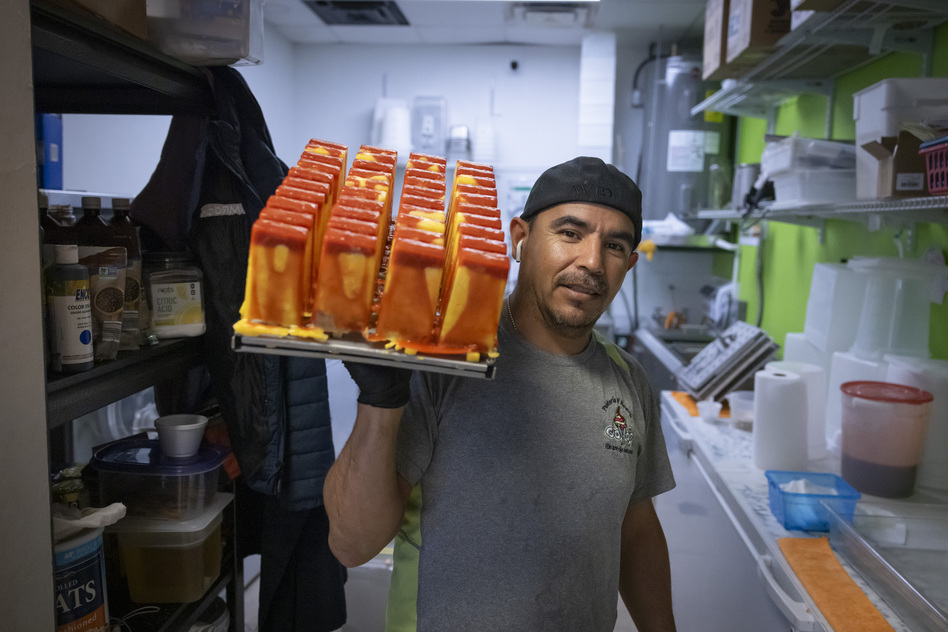 Manuel Vazquez, owner of Coya's artisan ice cream, poses for a photo as he carries a tray of ice pops in the kitchen of his shop in Fort Myers on Feb. 26, 2024. | Marco Bello for NPR