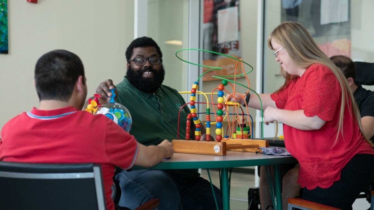 A support professional sits with three participants in sensory and cognitive activities at Pine Castle. l Aaron Mervin, Pine Castle