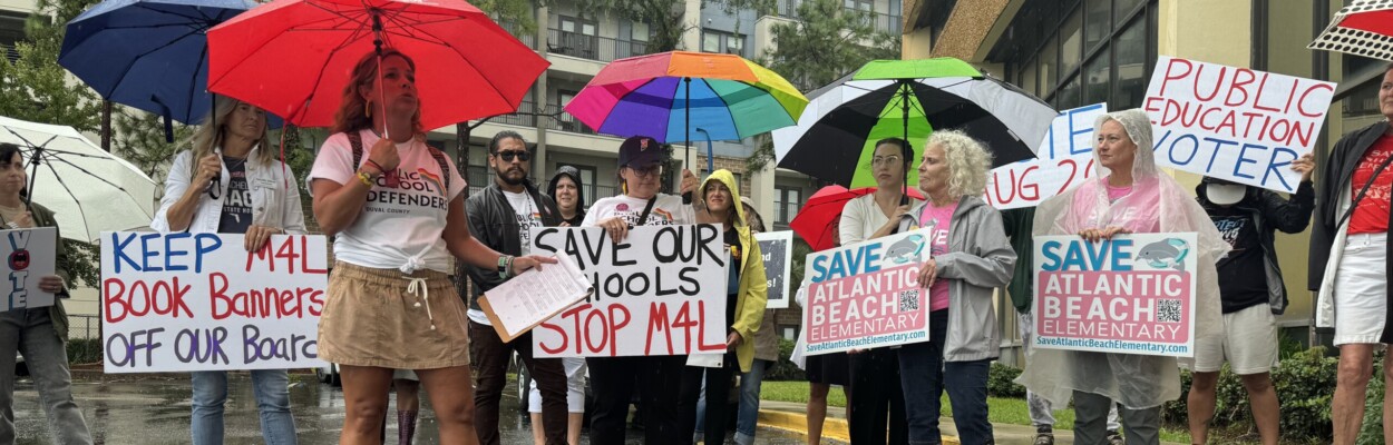 About two dozen people stand in the rain outside Duval school district headquarters on Tuesday, Aug. 6, 2024. The rally was organized by Public School Defenders and Families for Strong Public Schools, two Jacksonville advocacy groups. | Megan Mallicoat, Jacksonville Today