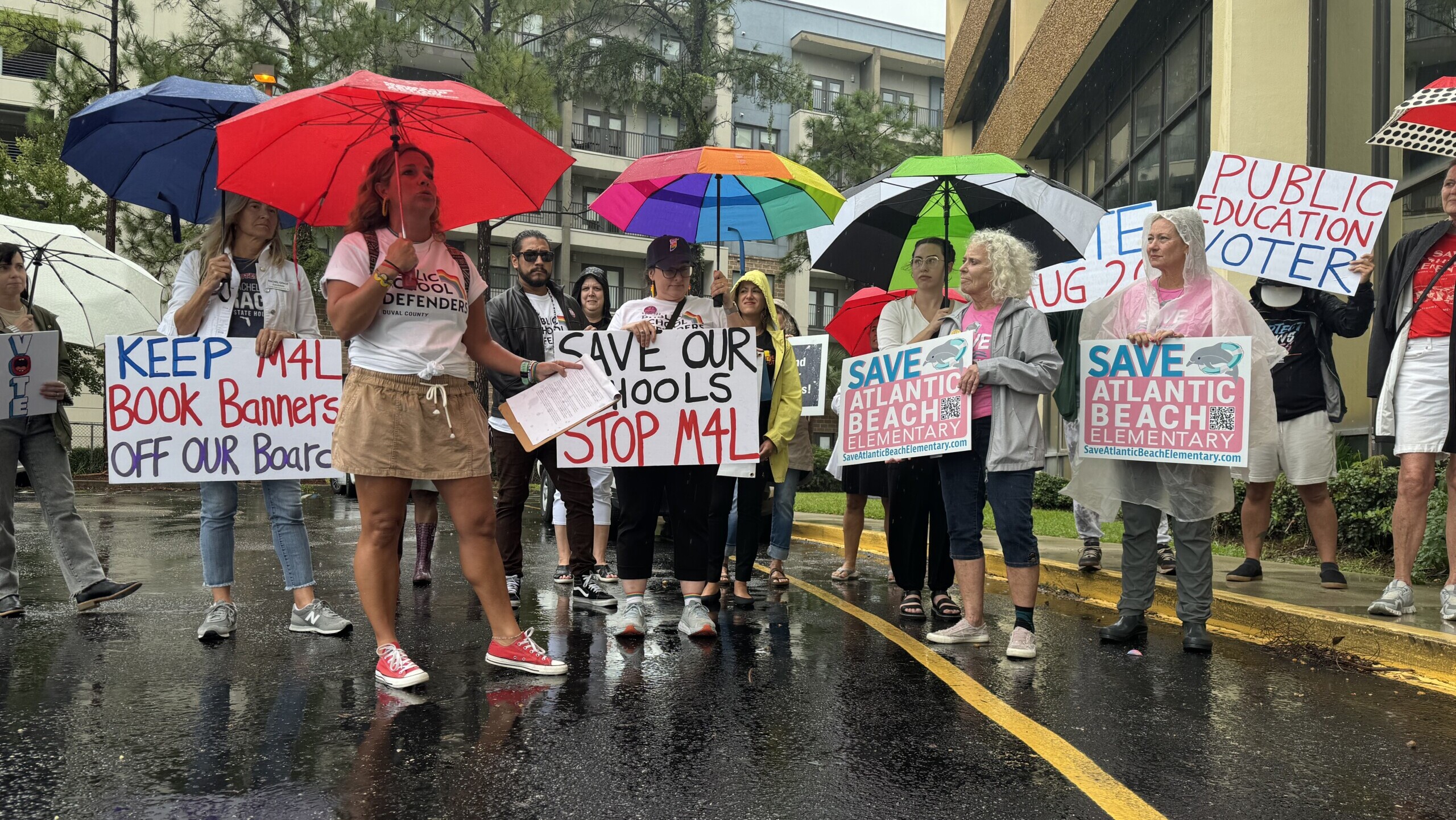 About two dozen people stand in the rain outside Duval school district headquarters on Tuesday, Aug. 6, 2024. The rally was organized by Public School Defenders and Families for Strong Public Schools, two Jacksonville advocacy groups. | Megan Mallicoat, Jacksonville Today