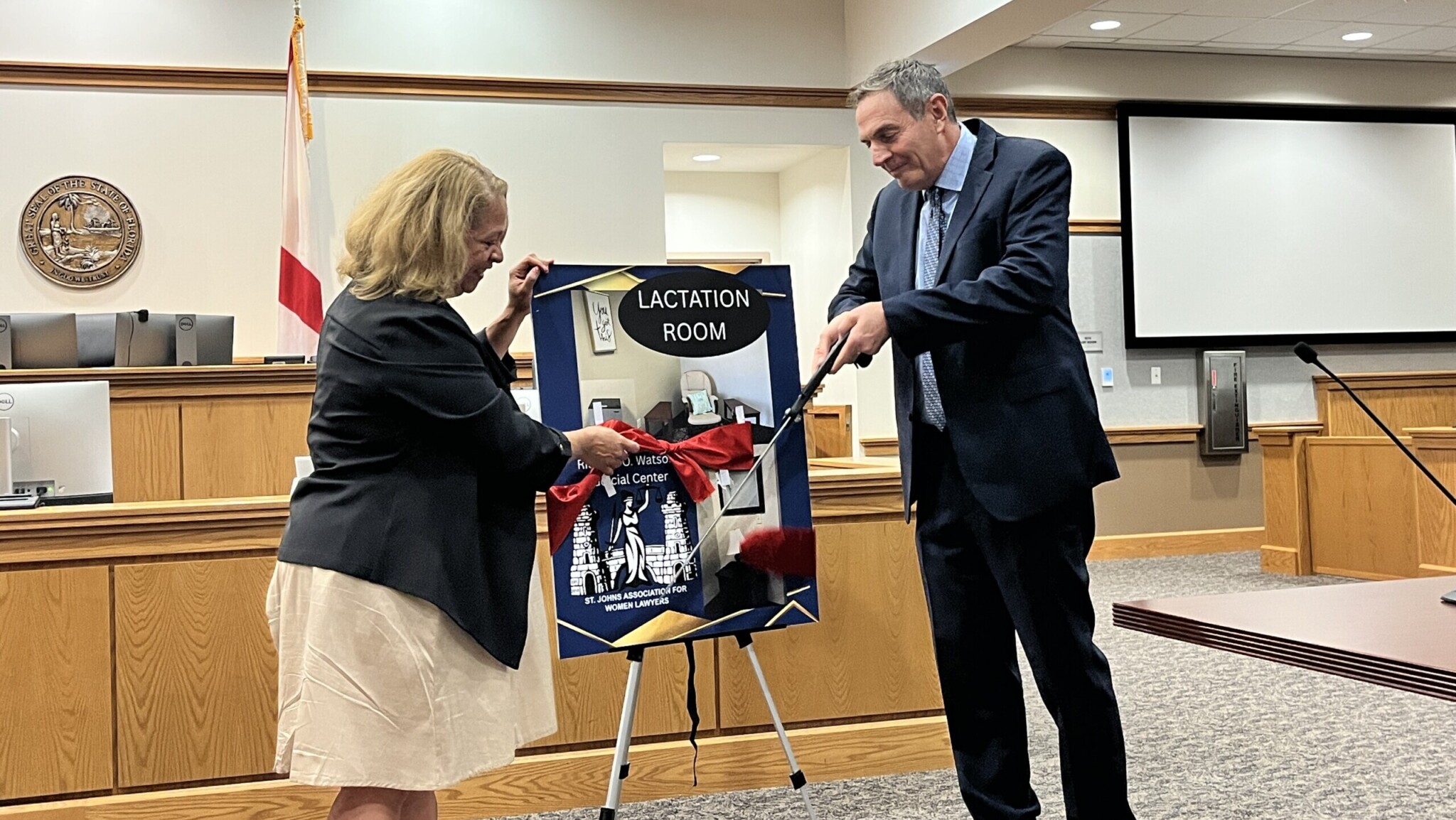 Ingrid Osborn, president of the St. Johns Association for Women Lawyers, and Circuit Judge Howard Maltz cut the ceremonial ribbon on a space for nursing and taking care of babies in the St. Johns County Courthouse