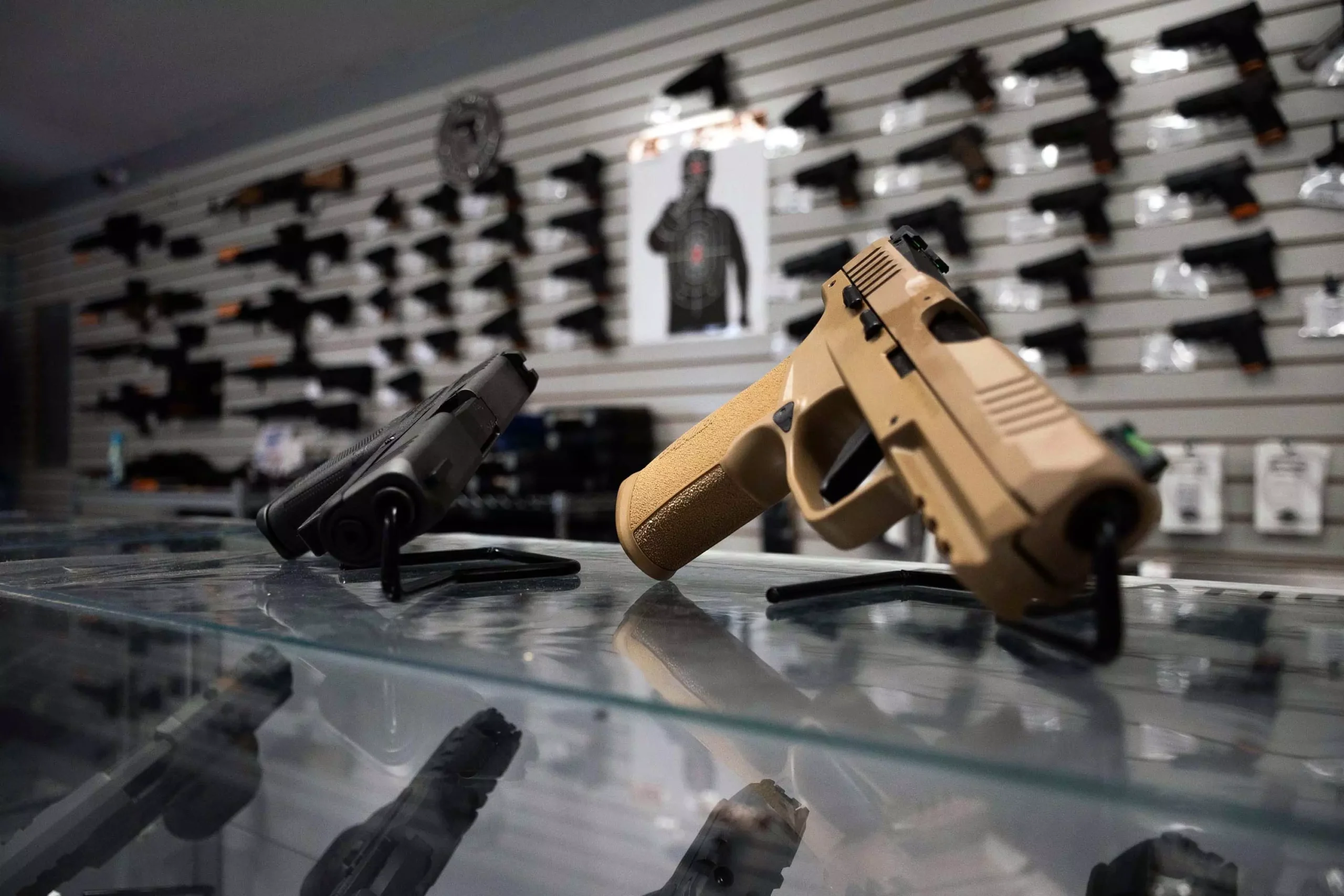 Two hand guns on top of a glass display. In the background are guns mounted on a wall.