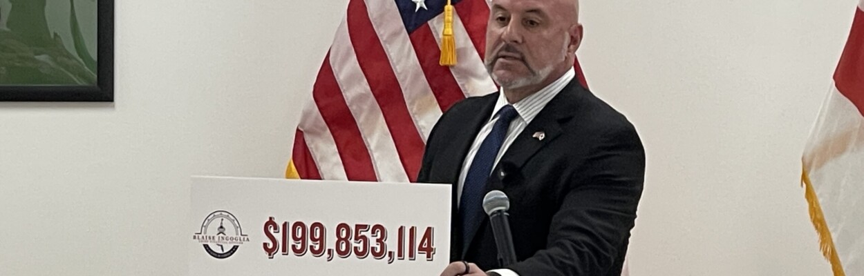 Florida's chief financial officer, Blaise Ingoglia, stands at a lectern during a Florida DOGE news conference in Jacksonville.