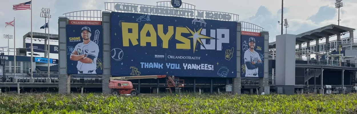 A large blue sign outside a stadium says Rays Up with players on either side