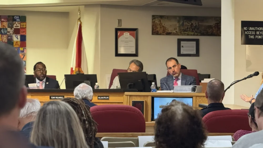 School Board lawyer sits on the dais and listens to public commenter speak