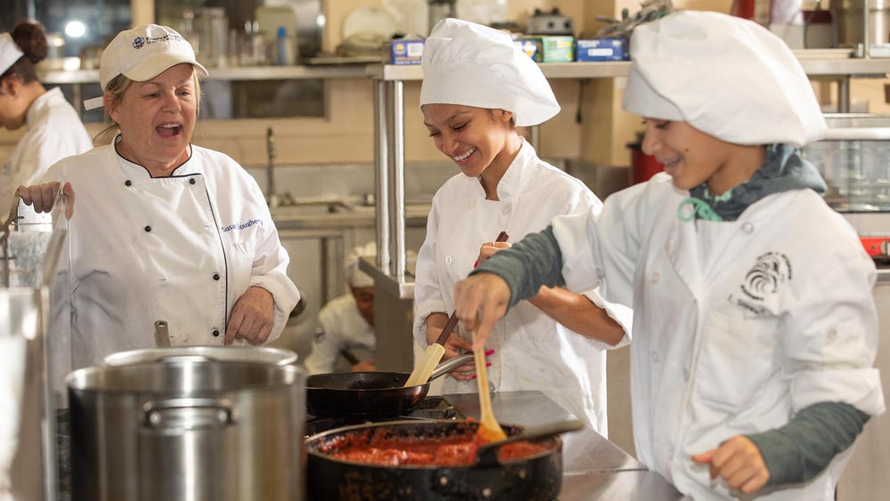 Two CTE students and their instructor stand at a stove cooking