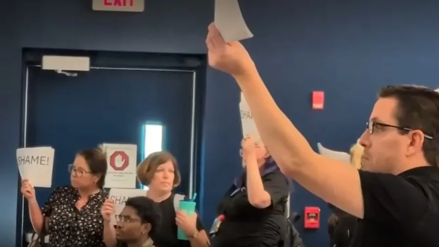 Teachers hold signs protesting at a School Board meeting