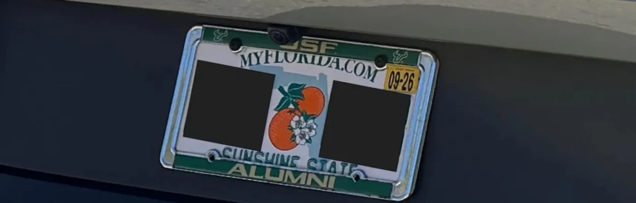 A closeup of a license plate on a vehicle. It has a steel, green and gold license plate frame that does not obscure the plate numbers.