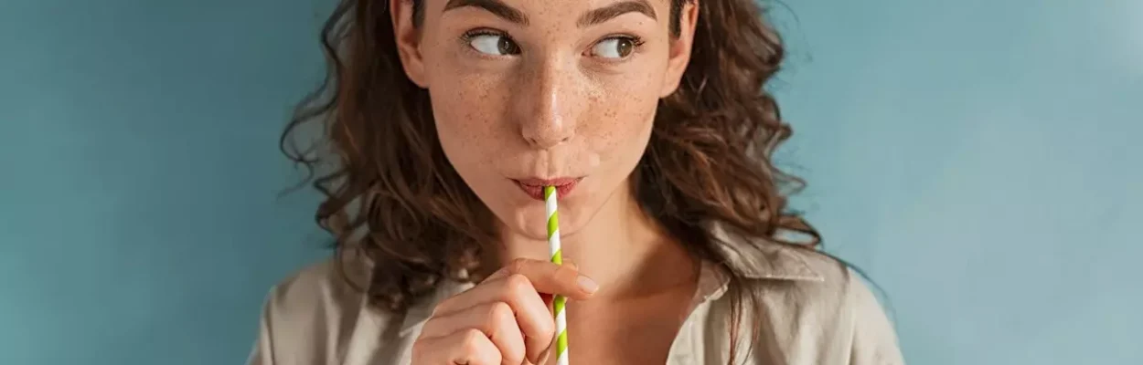 A young woman drinking a detox juice with a straw.