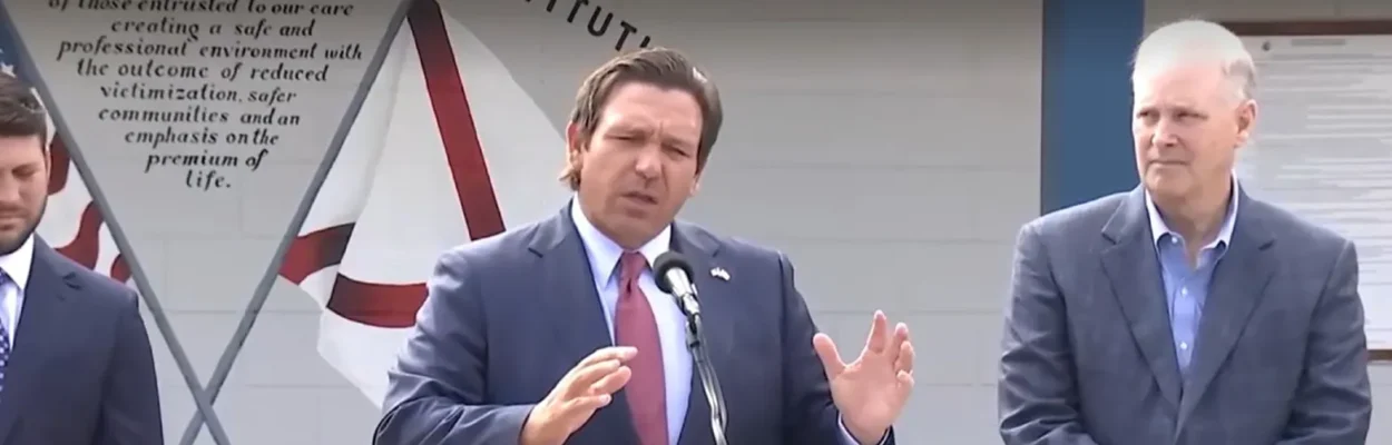Gov. Ron DeSantis speaking at a lectern at "Deportation Depot."