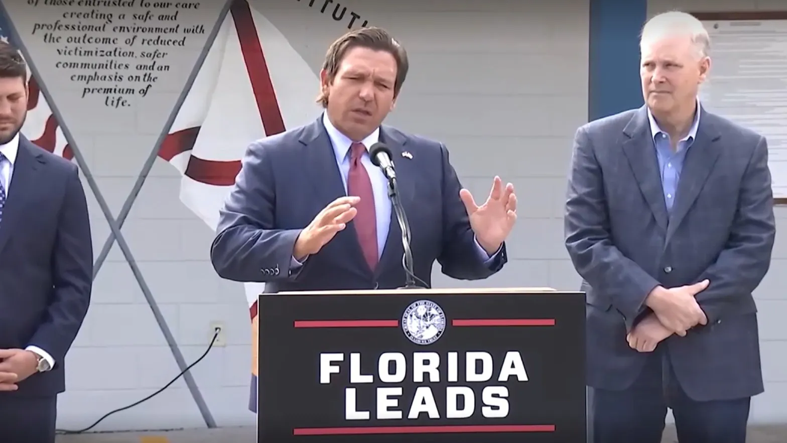 Gov. Ron DeSantis speaking at a lectern at "Deportation Depot."