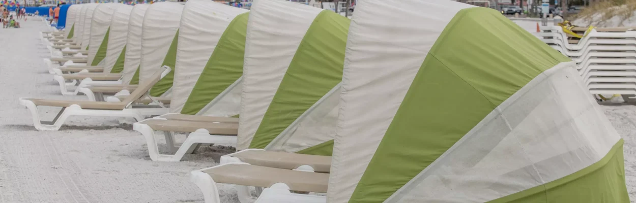 Green and white striped tents are lined along a beach for tourism.