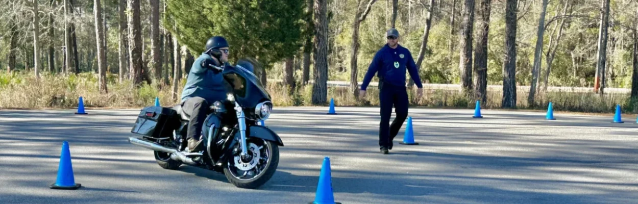 A motorcyclist weaves around blue cones during a motorcycle safety class.