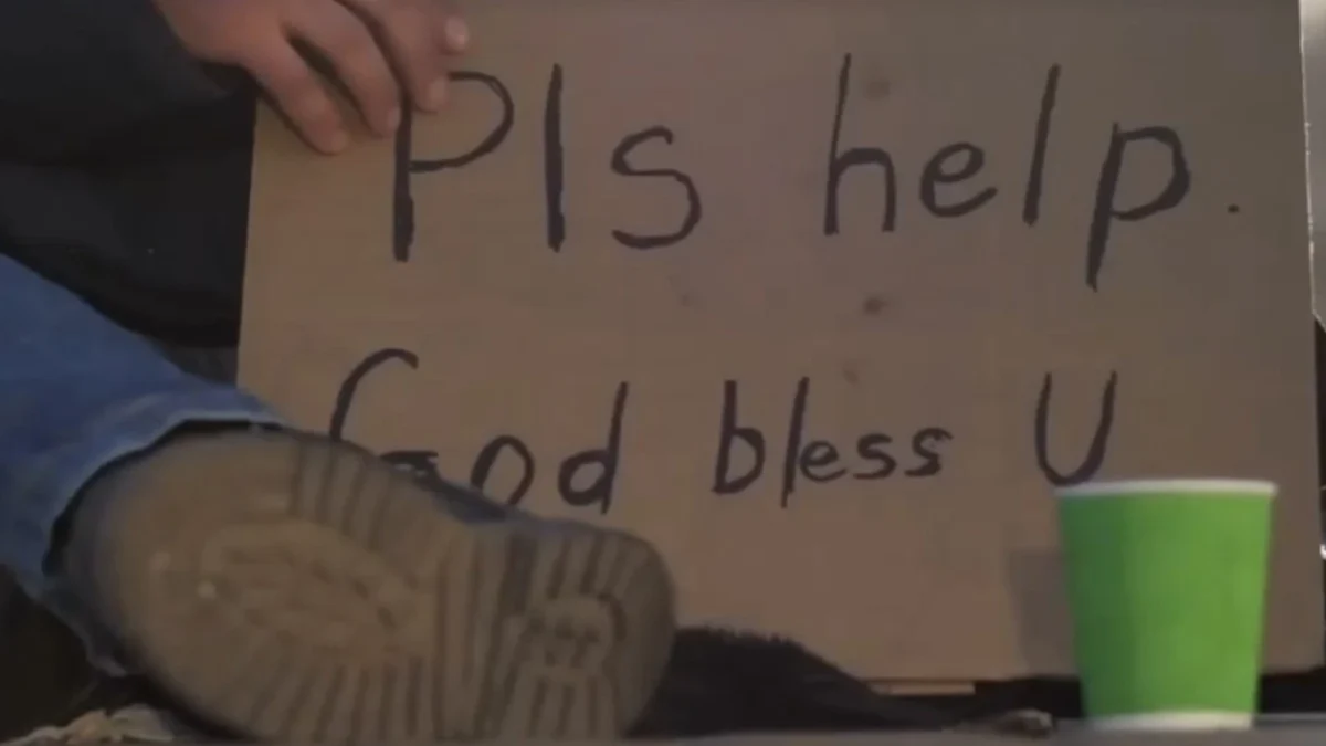 A man sits on the ground with a panhandling sign.