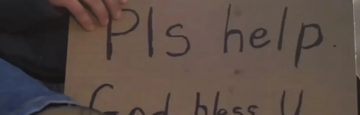 A man sits on the ground with a panhandling sign.