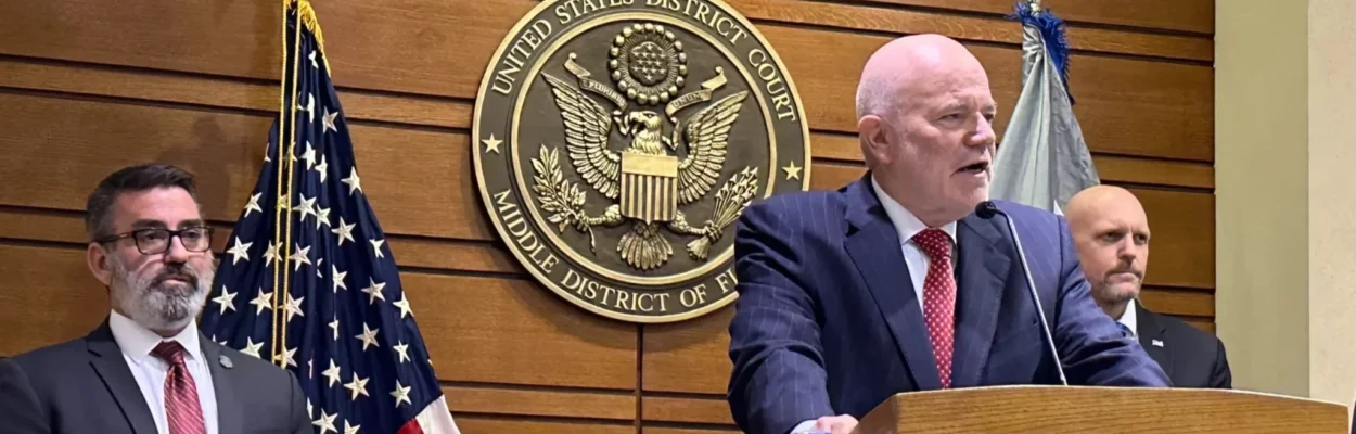 U.S. Attorney Gregory Kehoe standing at a lectern to explain an illegal scheme to obtain military access.