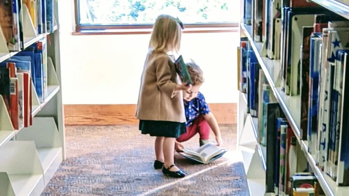 Two children stand among stacks of books