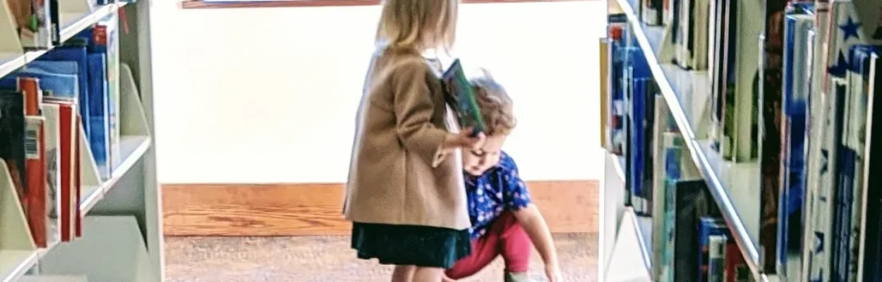 Two children stand among stacks of books