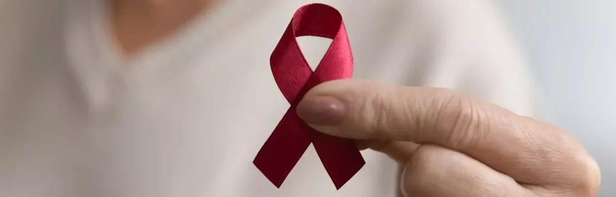A hand holds up a red ribbon as an HIV or AIDS awareness symbol