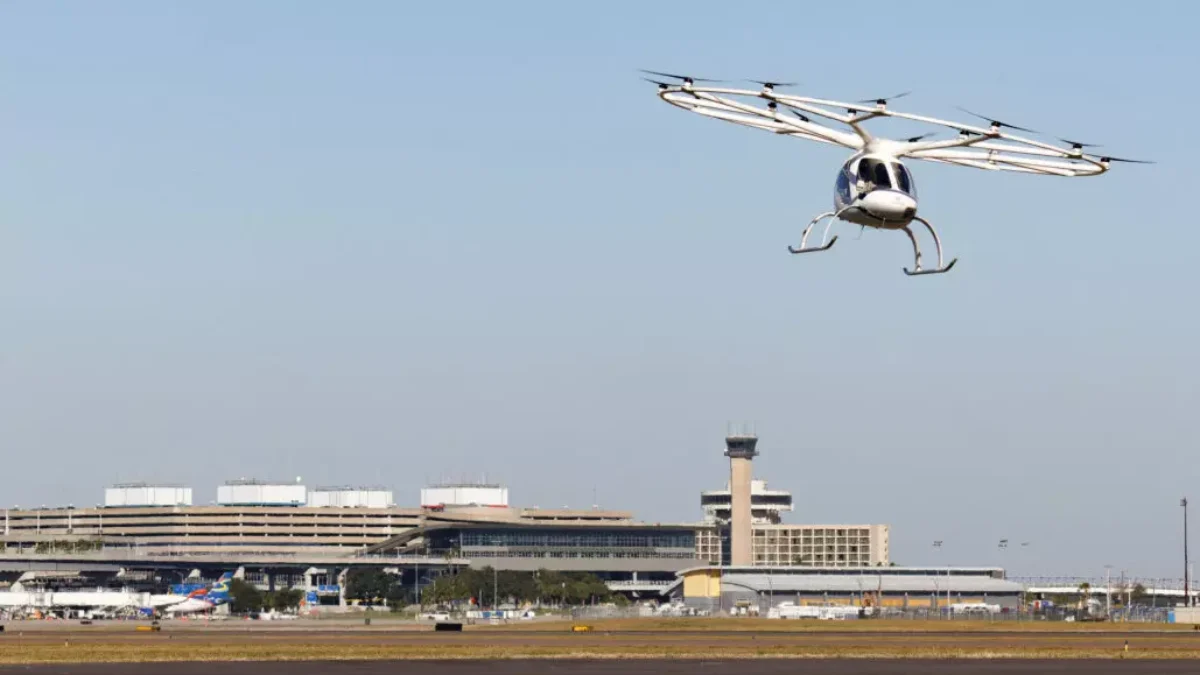 An air taxi flies over an airport terminal.