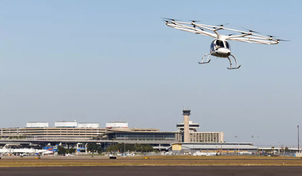 An air taxicab flies over an airport terminal.