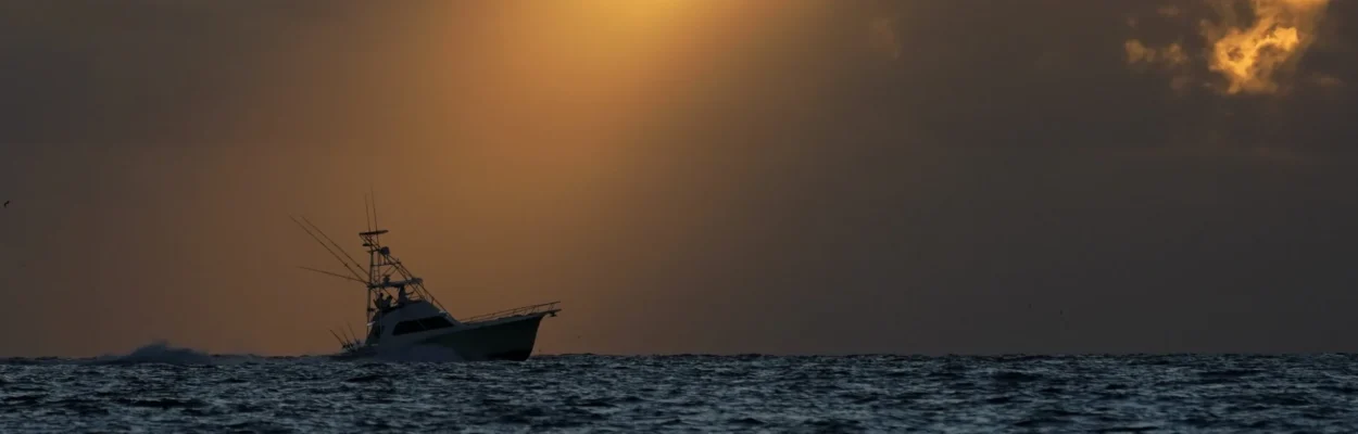 A fishing boat heading out to sea as the sun breaks through the clouds.