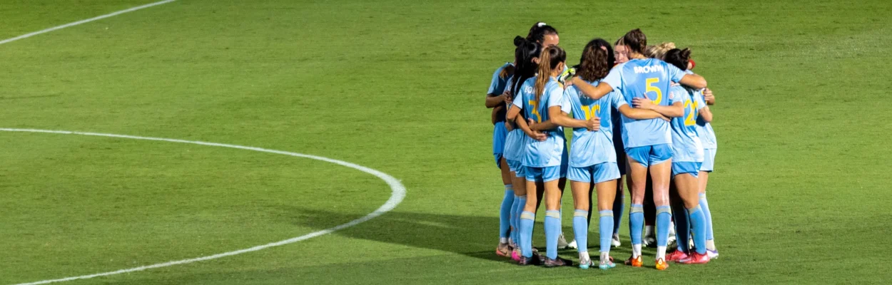 Members of the Sporting Jax Women's team huddle on the field.