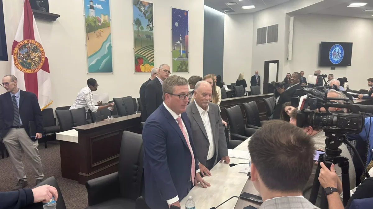 Florida legislative budget chairs surrounded by reporters in a Capitol committee room.