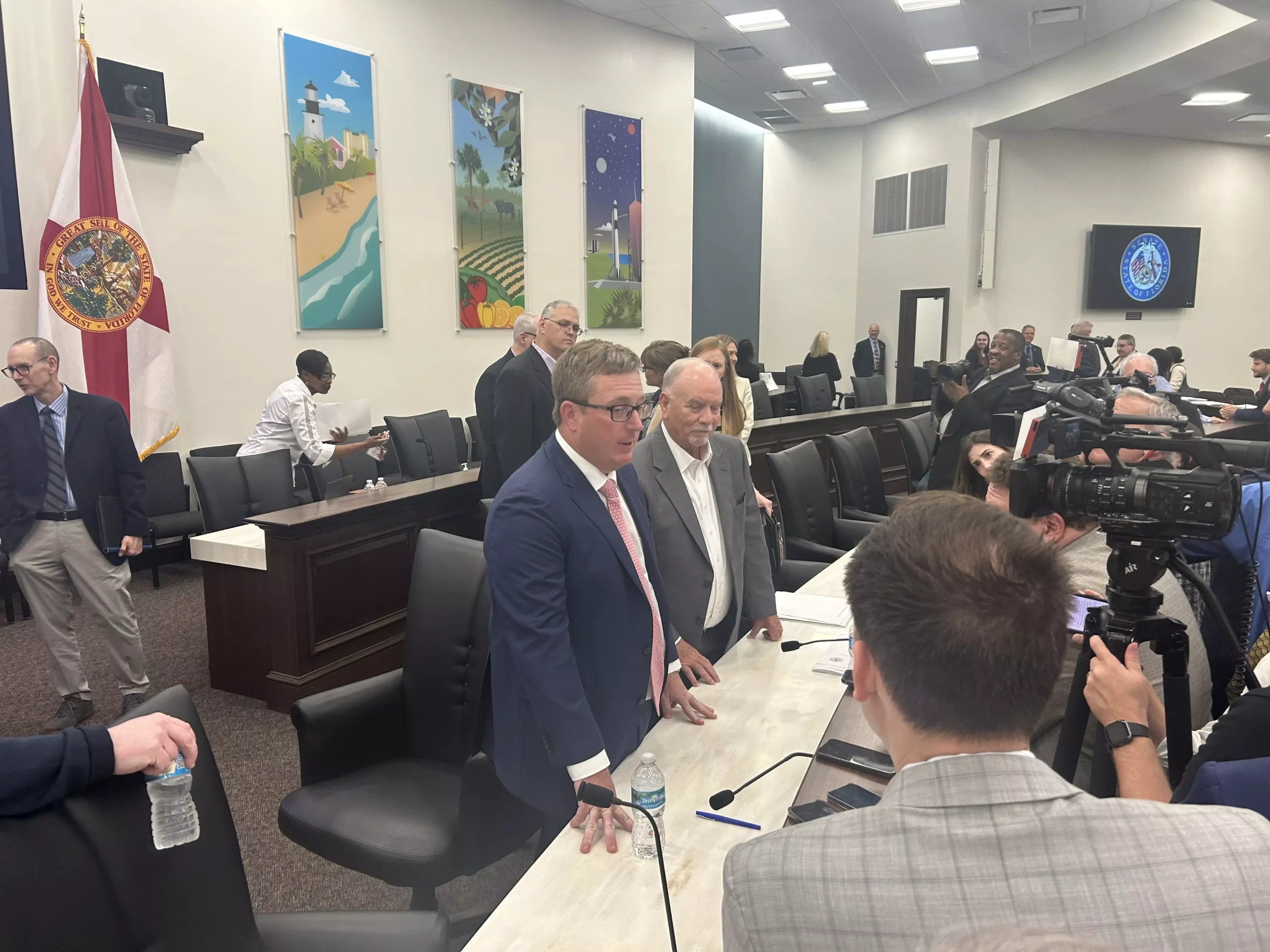 Florida legislative budget chairs surrounded by reporters in a Capitol committee room.