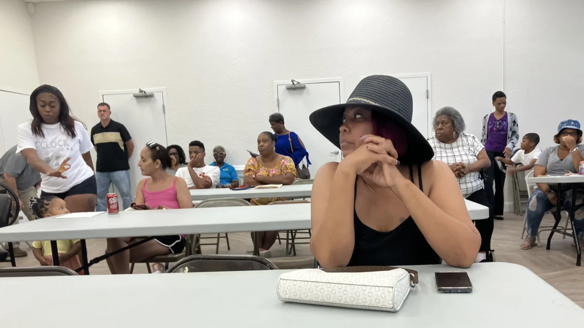 A woman sits at a table during a meeting about public housing, listening to what's being said.