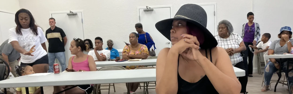 A woman sits at a table during a meeting about public housing, listening to what's being said.