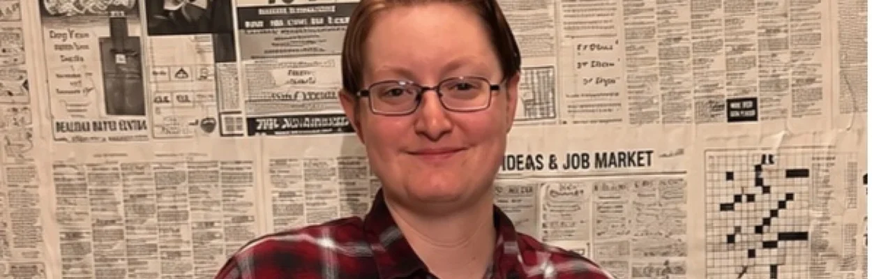 Teacher Shepard Scalf, an intersex man, poses in front of a wall of newspaper print.