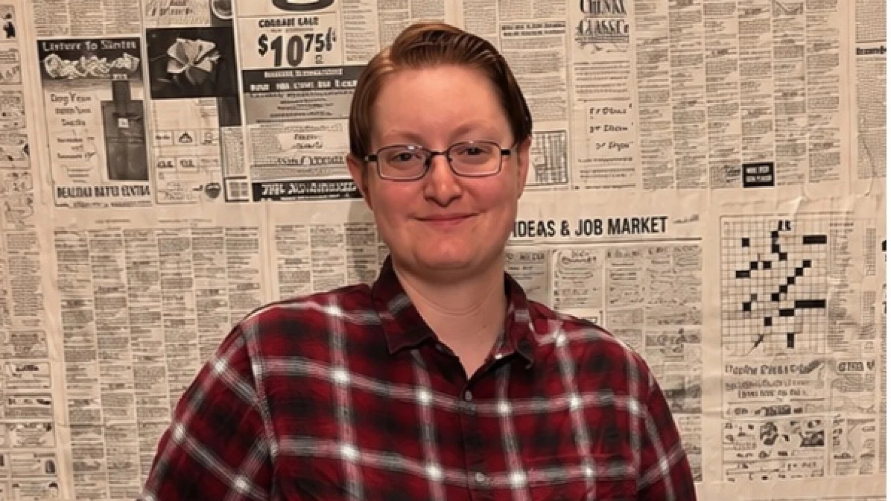 Teacher Shepard Scalf, an intersex man, poses in front of a wall of newspaper print.
