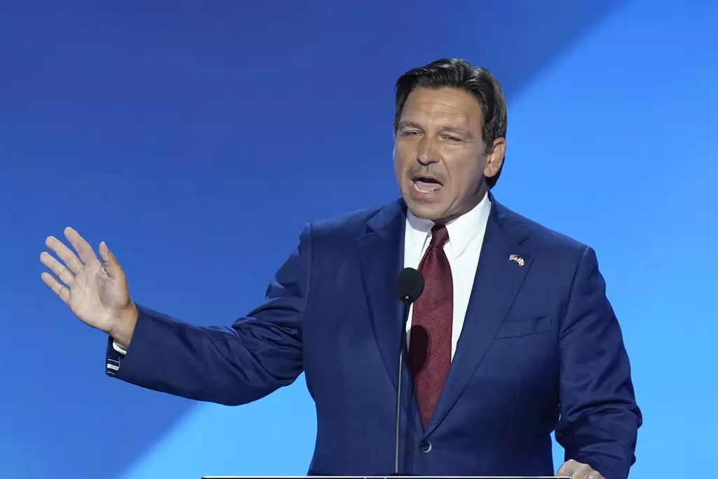 A man with brown hair wearing a blue suit and red tie speaking behind a microphone with his right hand raised in the air.