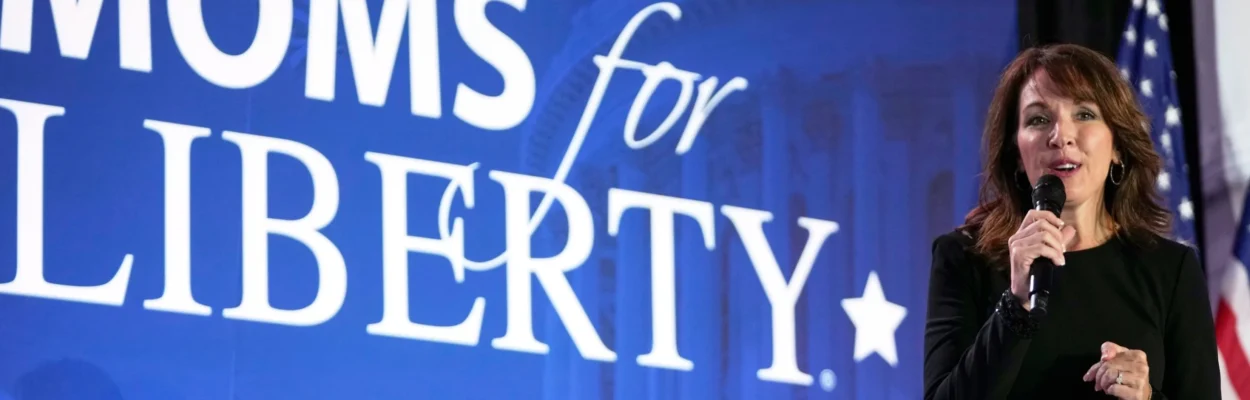 Moms for Liberty founder Tina Descovich holds a microphone while speaking in front of a Moms for Liberty banner.