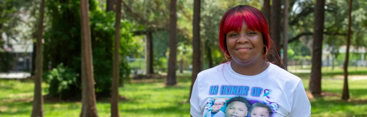 LaTiffany Gallion, founder of Austin's Voice, stands in a white T-shirt underneath trees at the Wiley Road Playground for a back-to-school giveaway.