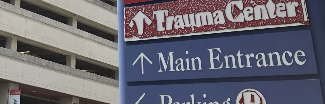 A sign points to the emergency room, trauma center, main entrance, and parking at a Miami hospital.