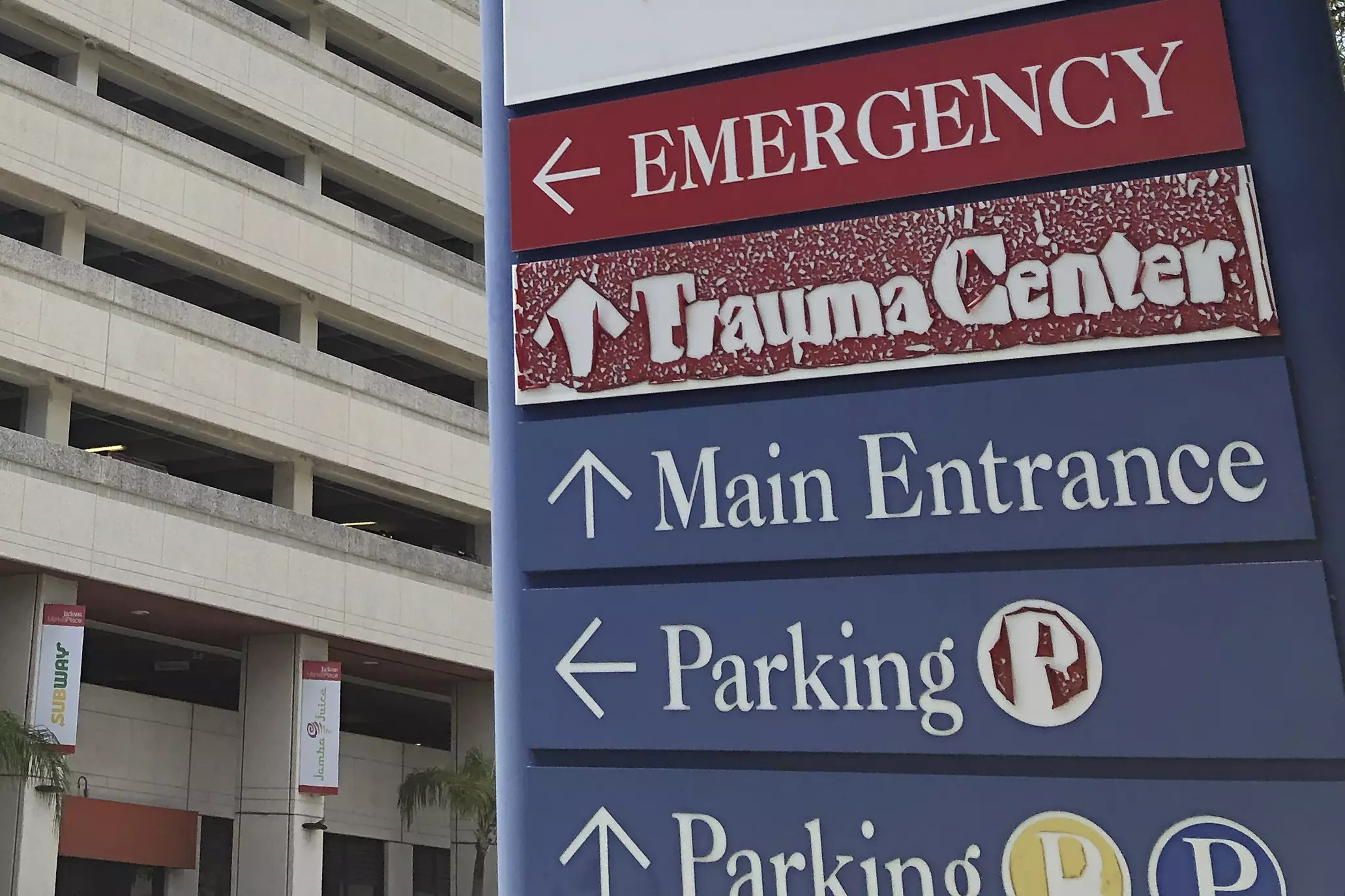 A sign points to the emergency room, trauma center, main entrance, and parking at a Miami hospital.
