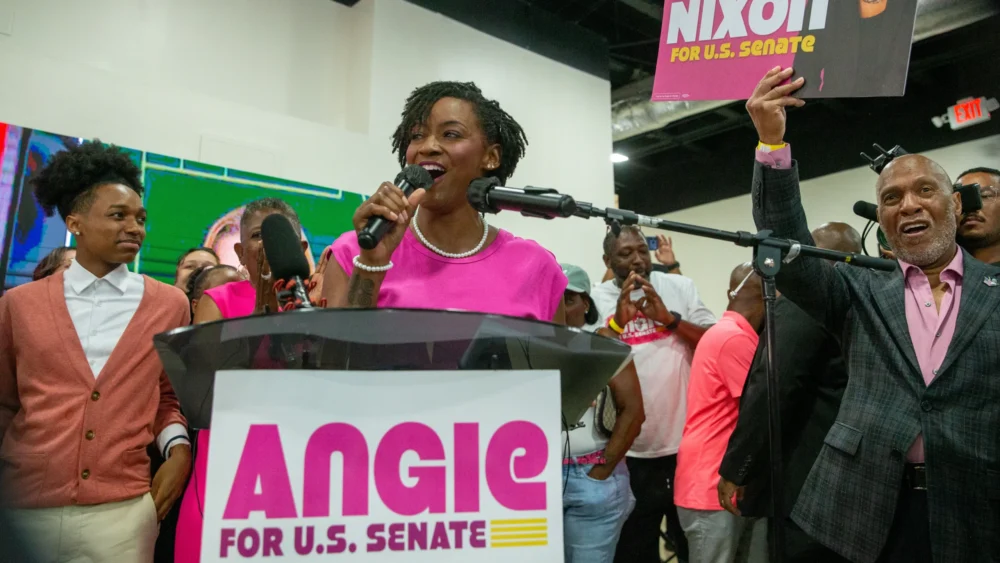 Angie Nixon speaks at podium surrounded by supporters