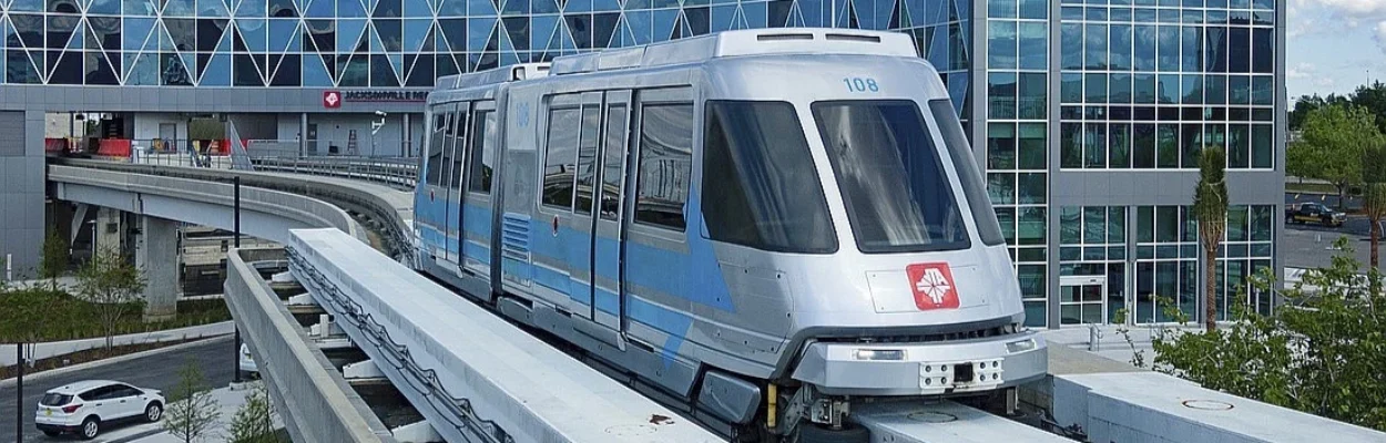 A Skyway train moving on a monorail, with the JTA headquarters in the background.